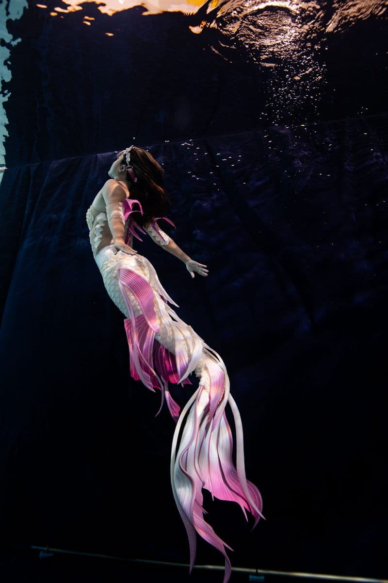 Mermaid swimmer in a white and pink tail underwater in a dark pool
