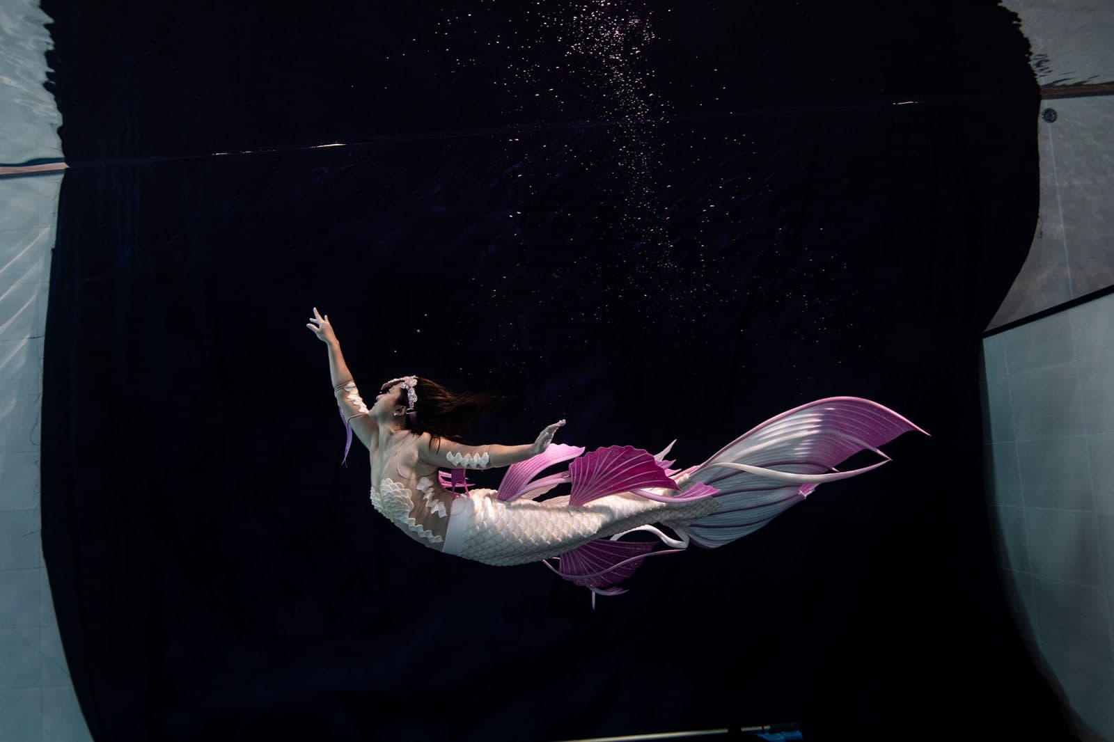 Mermaid swimmer gliding sideways through a dark pool