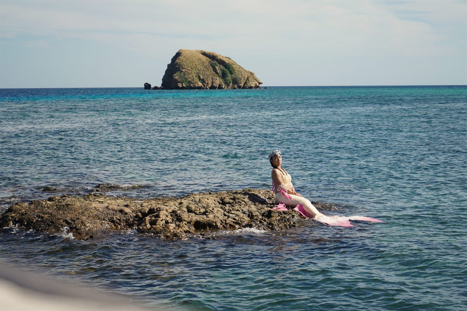 Mermaid swimmer sitting on ocean rocks beside blue water