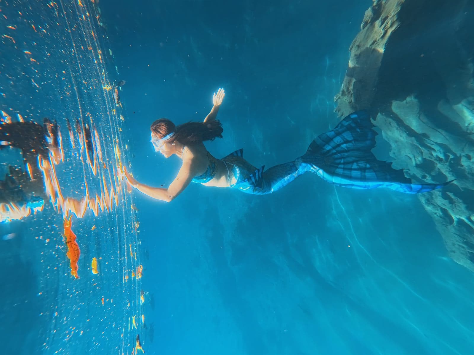 Mermaid swimmer floating in bright blue underwater light